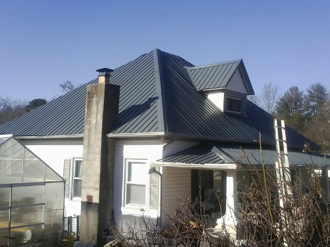 Dark blue standing seam metal roof on a white farmhouse with dormer — Slate & Tile Roof Repair by Roofing Brothers in Milldale