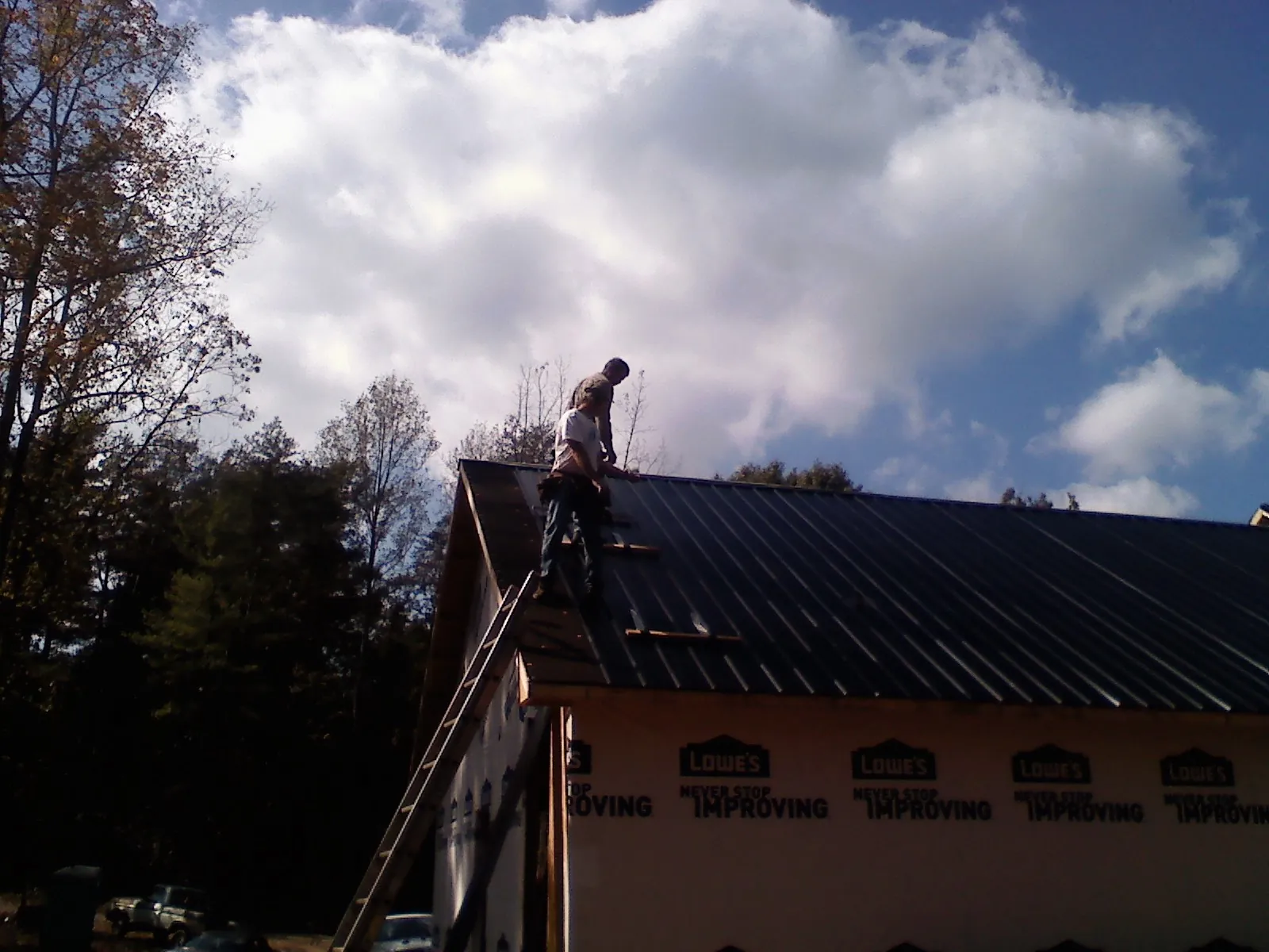 Roofer fastening dark metal panels high against a cloudy sky, from a Roof Inspection job in Milldale