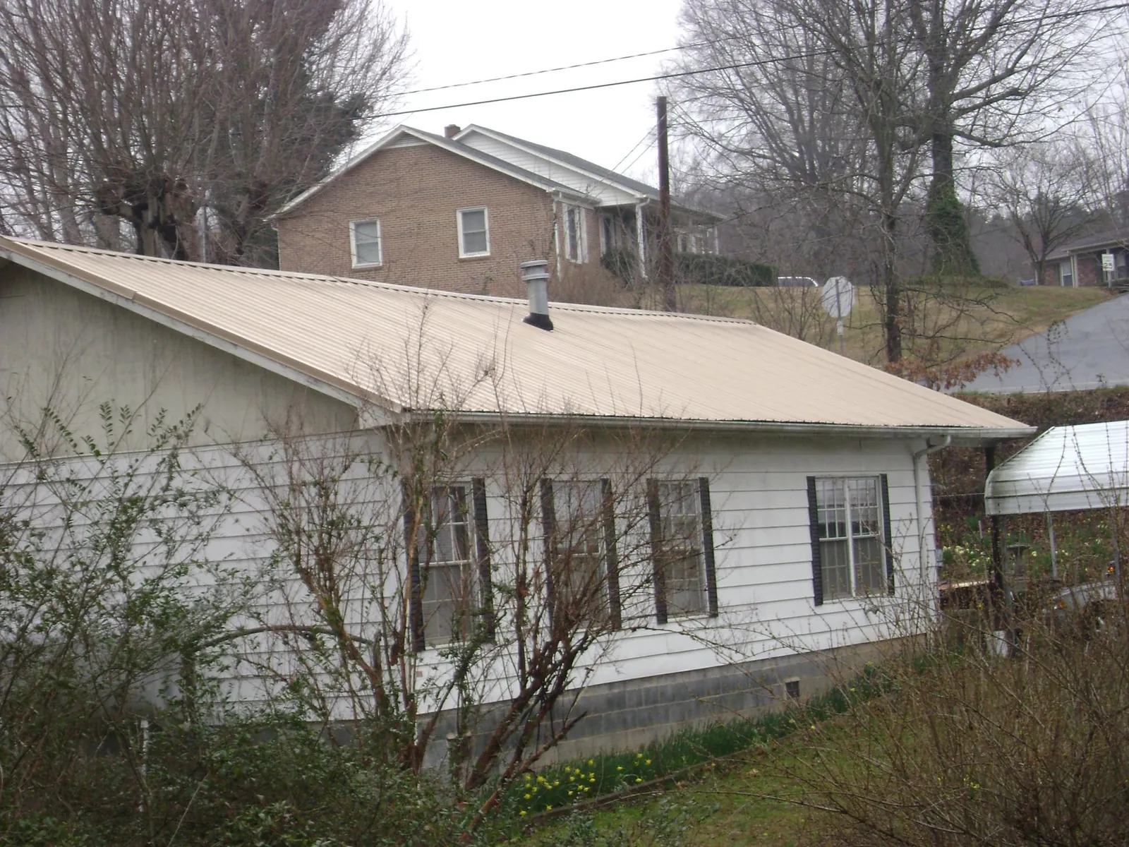 Tan metal roof on a white sided house set into a hillside — Commercial Roofing by Roofing Brothers in Milldale