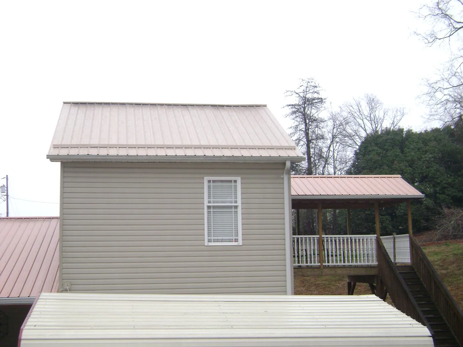 Tan metal roofs on a two story addition and attached porch, from a Roof Replacement job in Milldale
